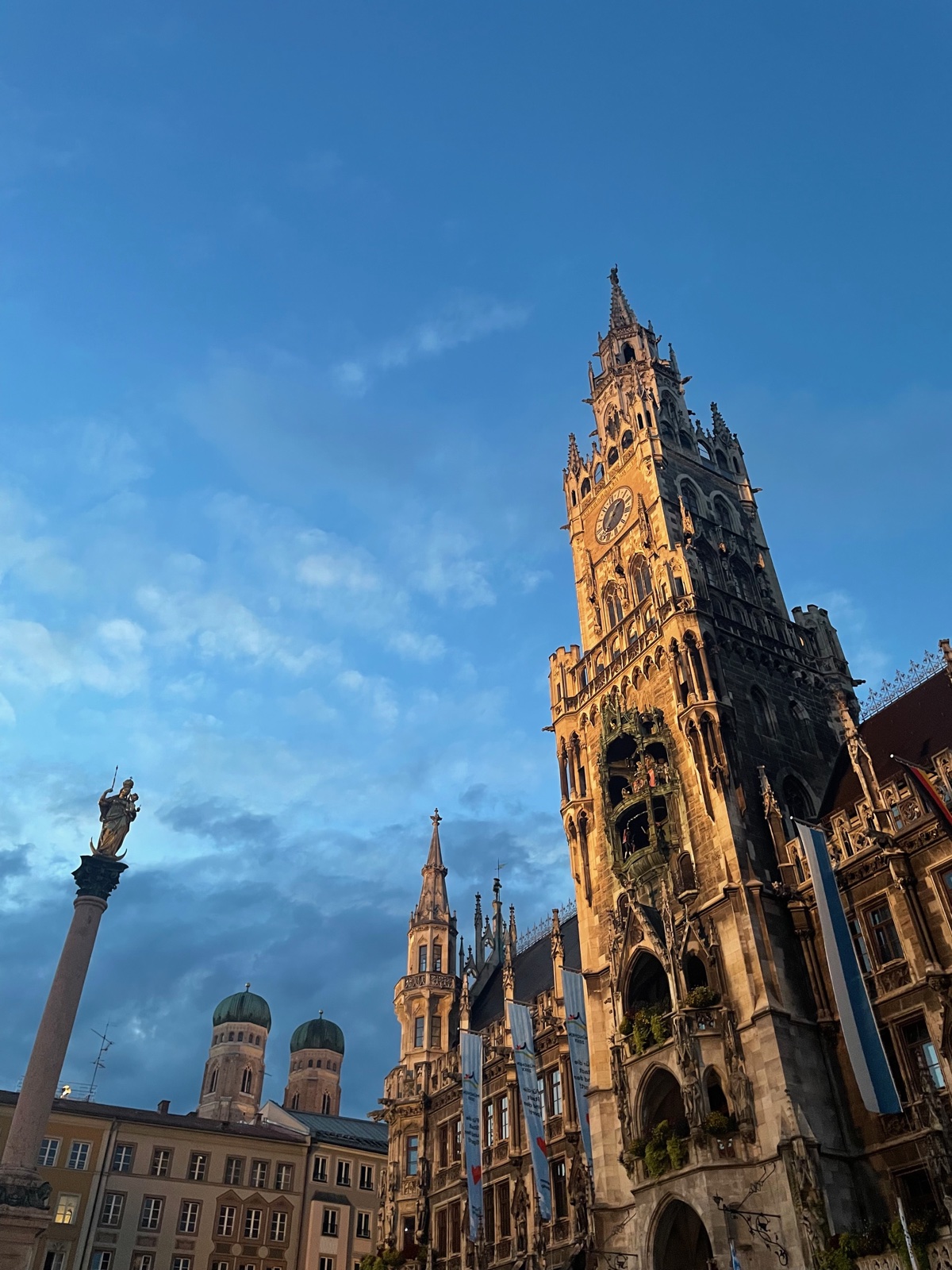 Munich’s New Town Hall tower glowing at sunset beside the Frauenkirche domes